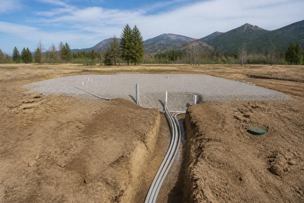 Diagram of site preparation steps for a manufactured home on land, featuring gravel pads and utility trenching.