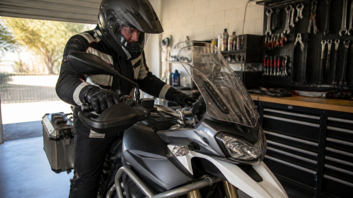 Motorcycle rider in protective gear inspecting adventure bike controls in a garage