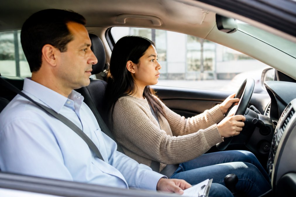 International student sitting in driver's seat during a lesson with a calm, professional DMV-certified instructor beside them, both focused on the road ahead, natural daylight through windshield