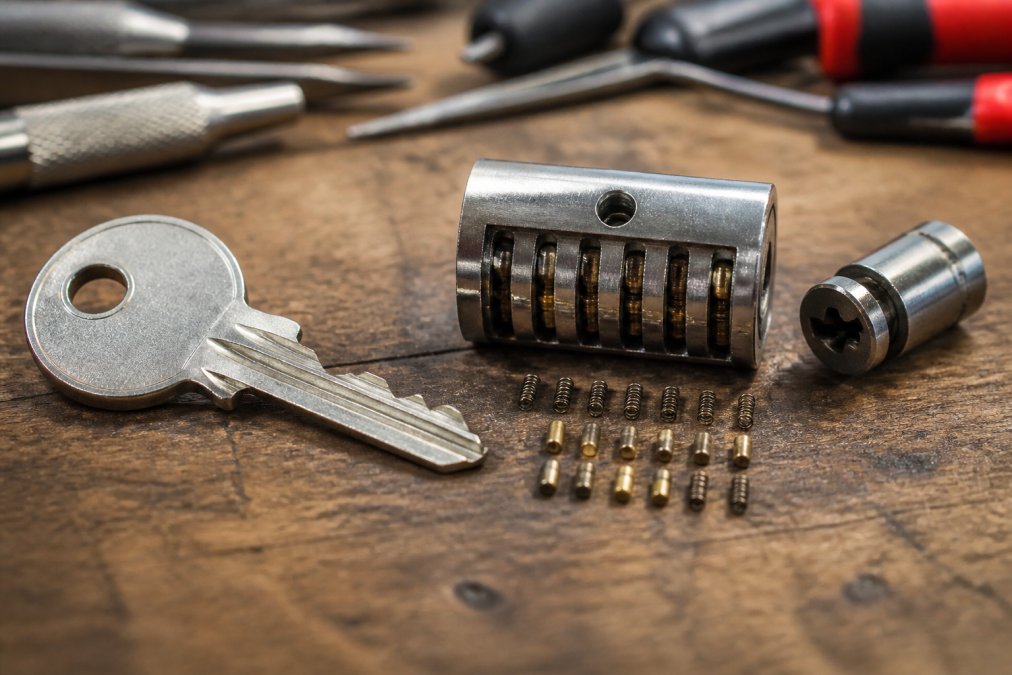 Close-up of a master key positioned next to an open cylinder plug showing internal pin tumbler components and springs arranged on a workbench with professional locksmith tools