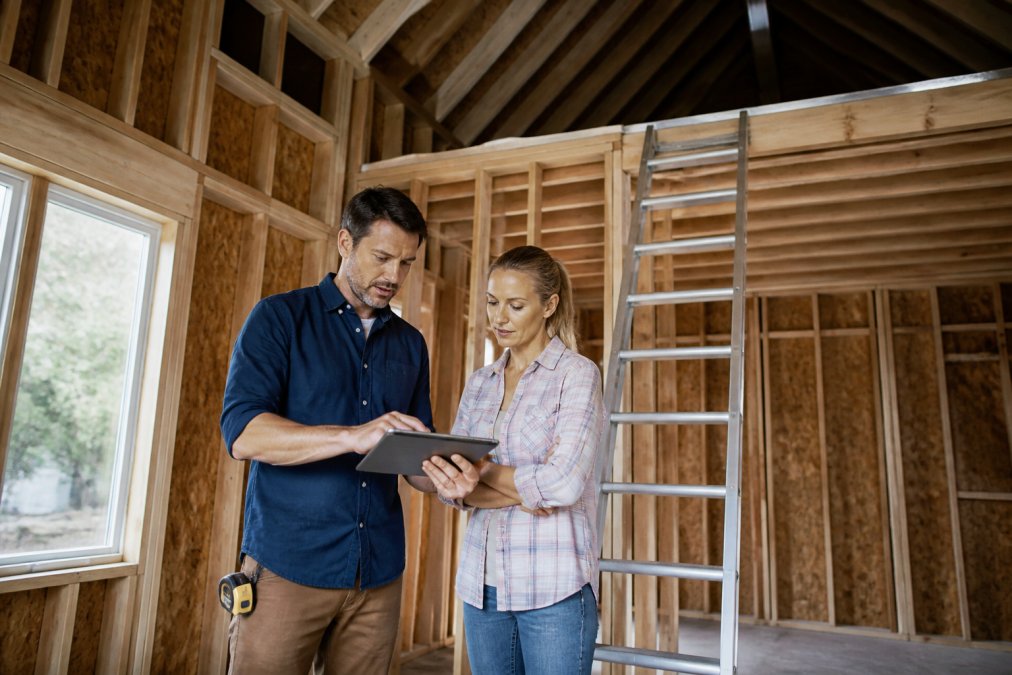 Engineer and homeowner reviewing loft blueprints inside a detached ADU under construction with exposed joists