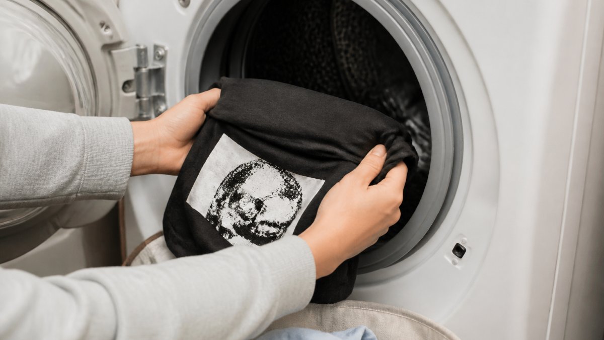 Hands gently turning a graphic t-shirt inside-out before placing it in a washing machine, showing careful handling of the printed design