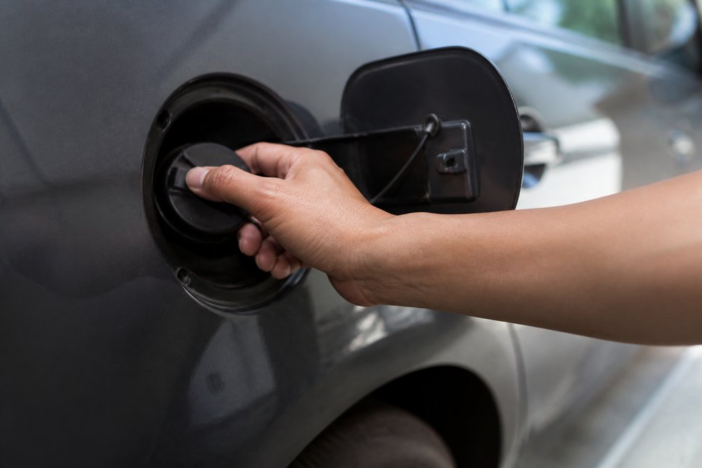 Hands tightening a vehicle's gas cap with the fuel door open, showing the cap being firmly secured onto the fuel filler neck