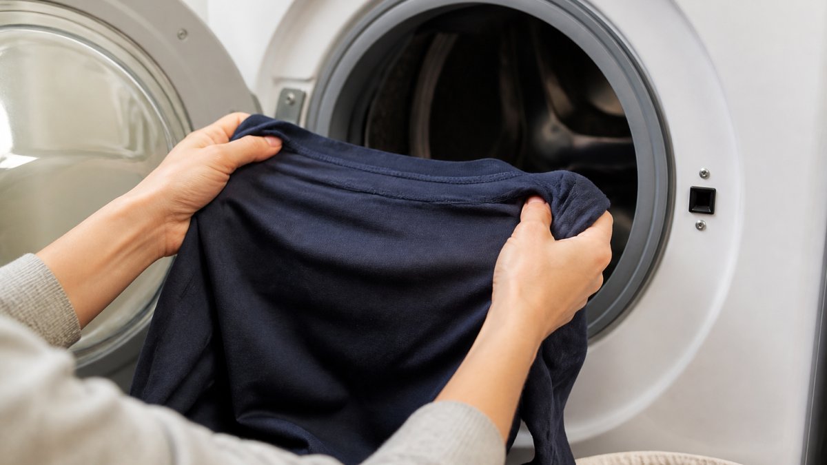 Close-up of hands turning a screen-printed shirt inside out before placing it in a washing machine, showing proper care technique with natural lighting