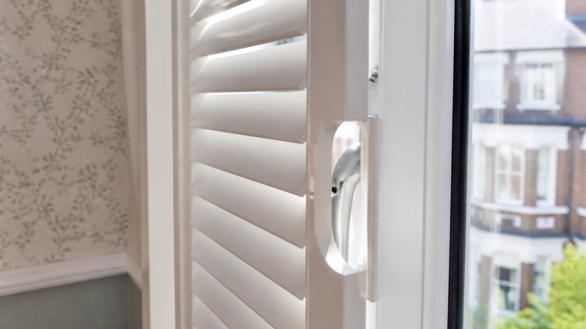 White plantation shutters fitted to inward opening windows in a period London home with sunlight filtering through.