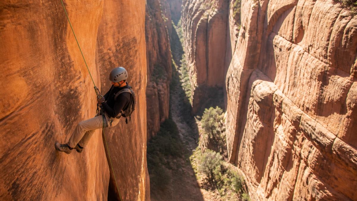 Climber rappelling down a narrow sandstone canyon wall using a static rope in the afternoon light