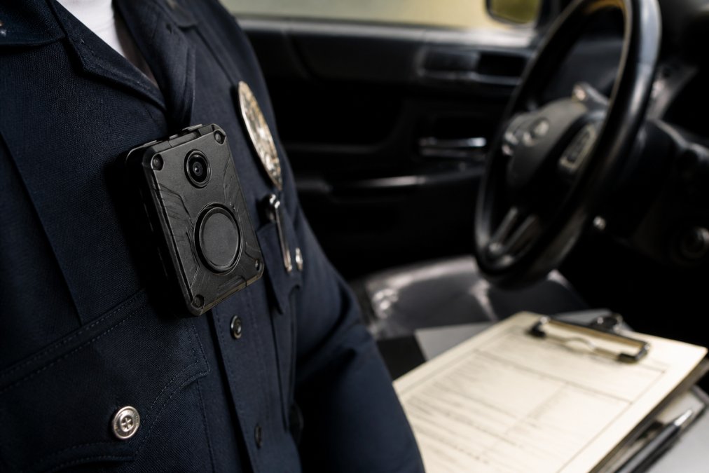 Close-up of a police officer's body camera mounted on uniform chest, citation pad visible on dashboard, representing evidence documentation and procedural accountability in law enforcement