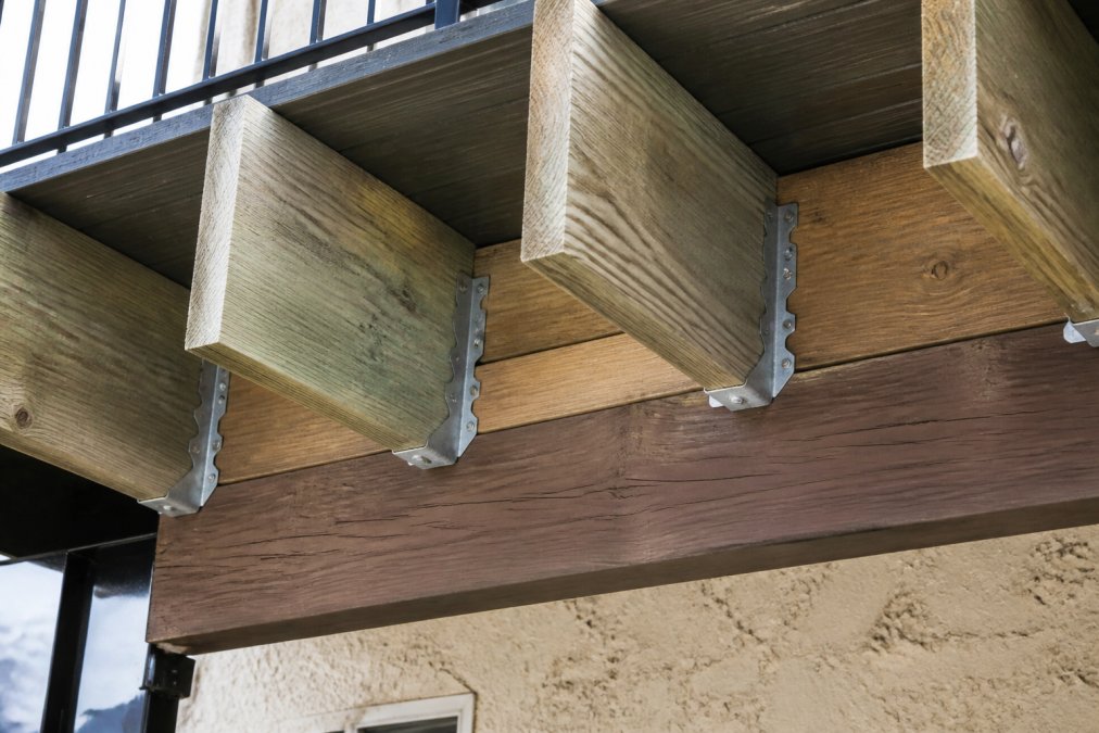 Close-up view from below of a cantilevered deck frame showing pressure-treated joists extending past a support beam, with galvanized joist hangers and solid blocking visible between the joists