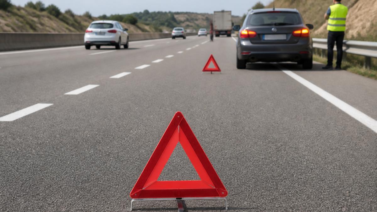 Car Breaks Down in Spain: Step-by-Step Safety Guide Driver in high-visibility vest stands behind barrier after a car breaks down in Spain on a busy motorway.
