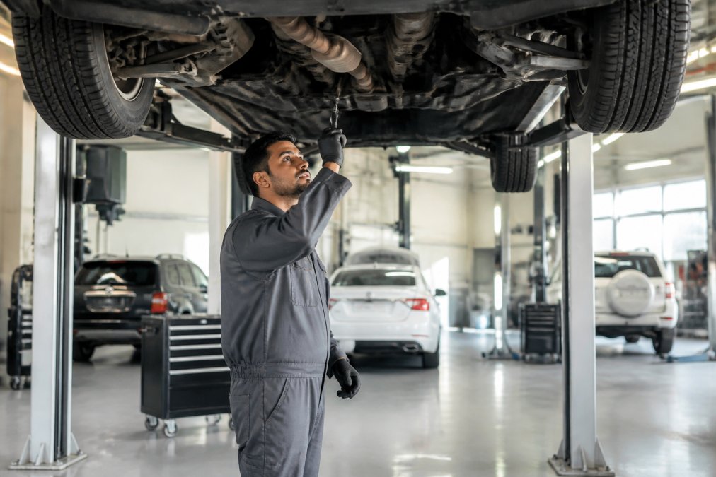A modern car service center in Dubai with a vehicle raised on a lift, a technician in a clean uniform inspecting the undercarriage, bright workshop lighting