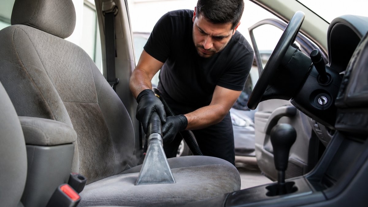 Professional detailer using specialized steam extraction equipment on car upholstery, concentrating on a heavily soiled fabric seat with focused intensity