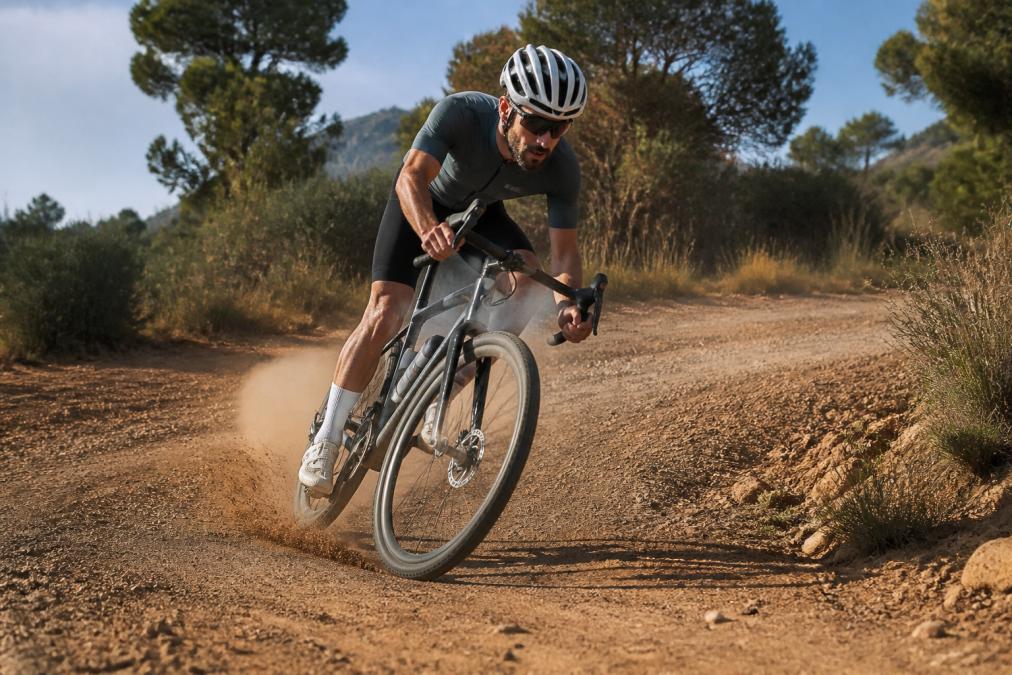 Competitive gravel racer on dusty terrain, leaning into a hard corner with focus on the carbon wheelset and bike handling, showing speed and control in natural outdoor lighting