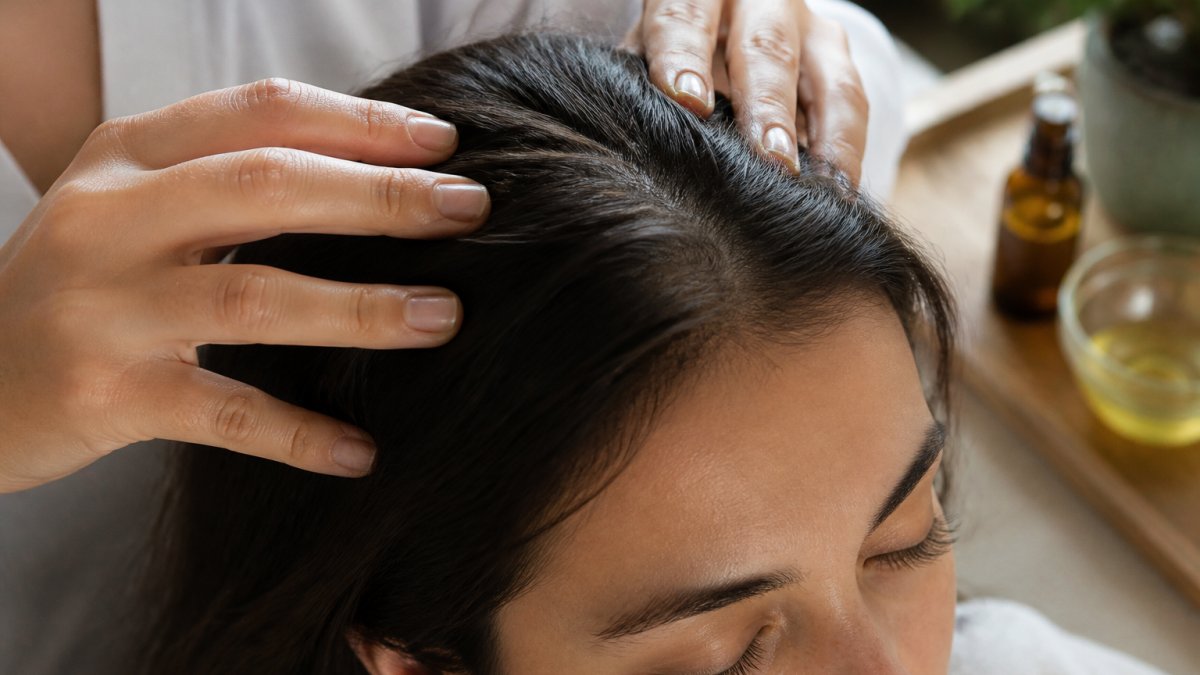 Close-up of a person's scalp receiving a gentle oil massage with fingertips, showing calm focus and healthy scalp care routine
