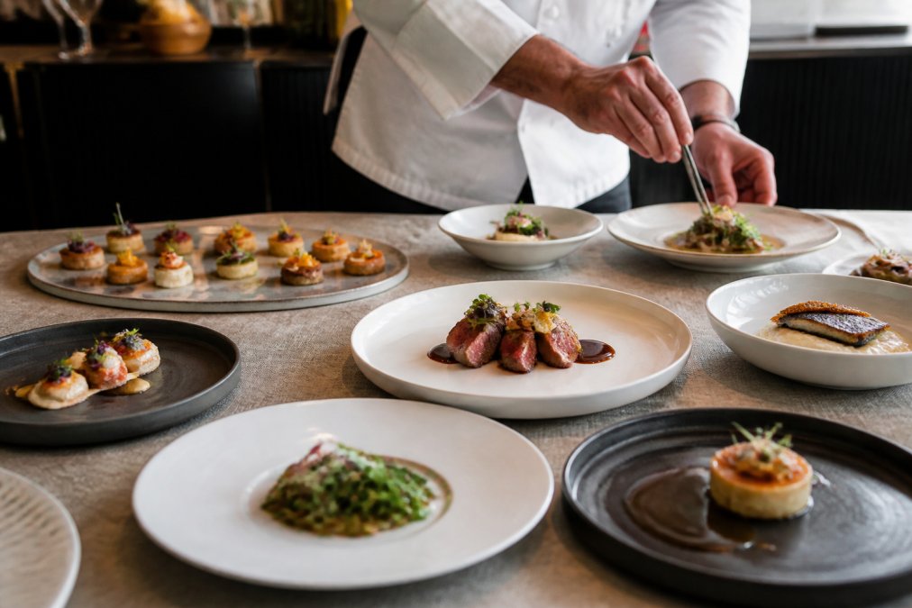Elegantly plated five-course meal with gourmet hors-d'oeuvres displayed on fine china and minimalist white plates, showcasing professional culinary presentation with artistic food arrangement at a luxury gala