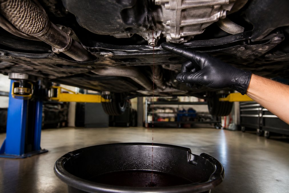 Mechanic pointing to a red transmission fluid leak dripping from the underside of a car transmission pan