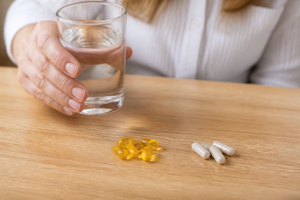 Person holding a glass of water with a CBD softgel capsule visible, representing the ingestion and absorption process in a wellness context