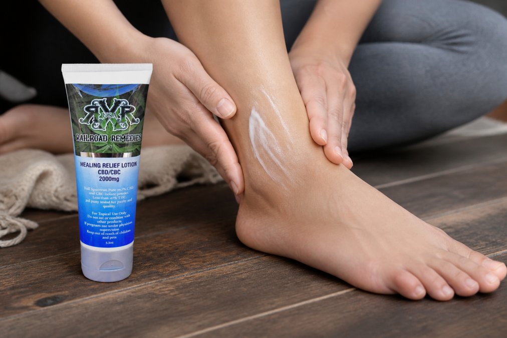 Close-up of hands gently massaging CBD cream lotion into the foot and ankle area in warm natural lighting, demonstrating proper circular massage technique on skin
