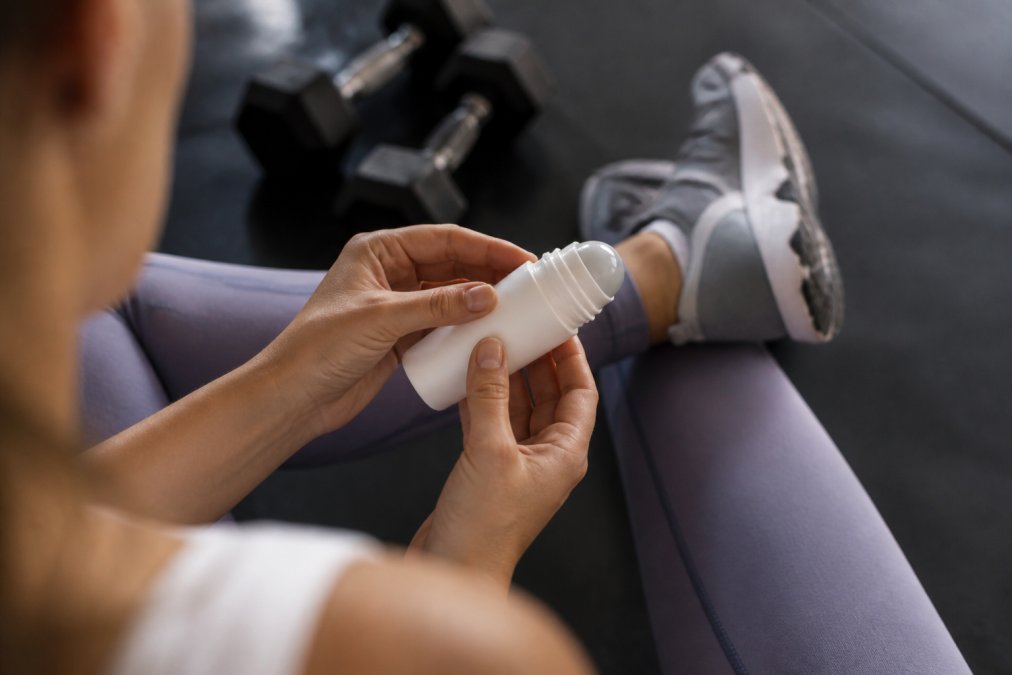 Close-up of hands holding a CBD freeze gel roll-on applicator with athletic wear visible in background, representing targeted pain relief for active individuals in recovery