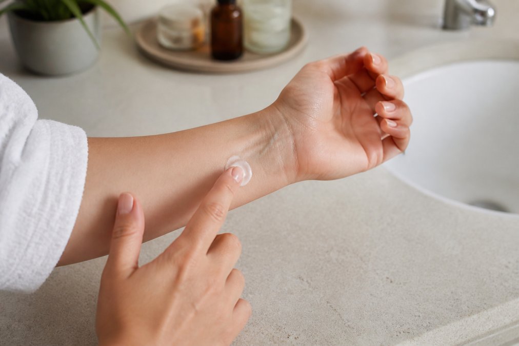 Close-up of an adult's inner forearm with a small dab of cream being applied near the wrist, soft natural light, clean bathroom counter in background
