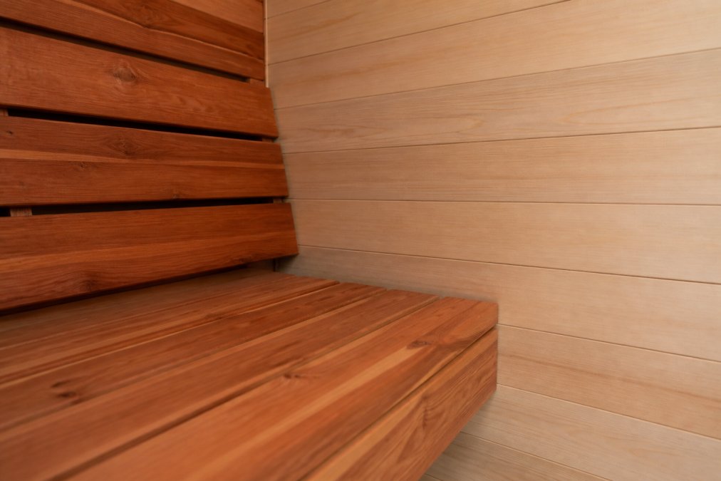 Close-up of a sauna interior showing cedar's warm reddish-brown grain on one bench and hemlock's pale, uniform texture on the adjacent wall panels, soft ambient lighting