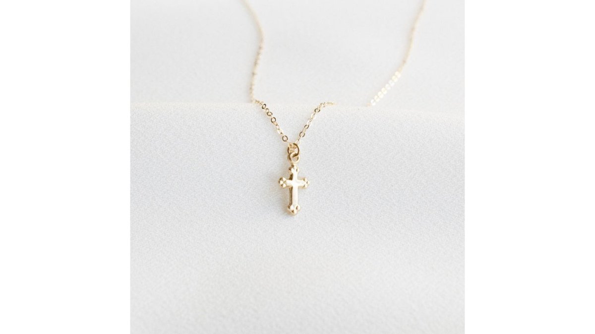Woman wearing an elegant gold plated cross necklace layered with other delicate chains, styled for everyday sophistication in natural daylight