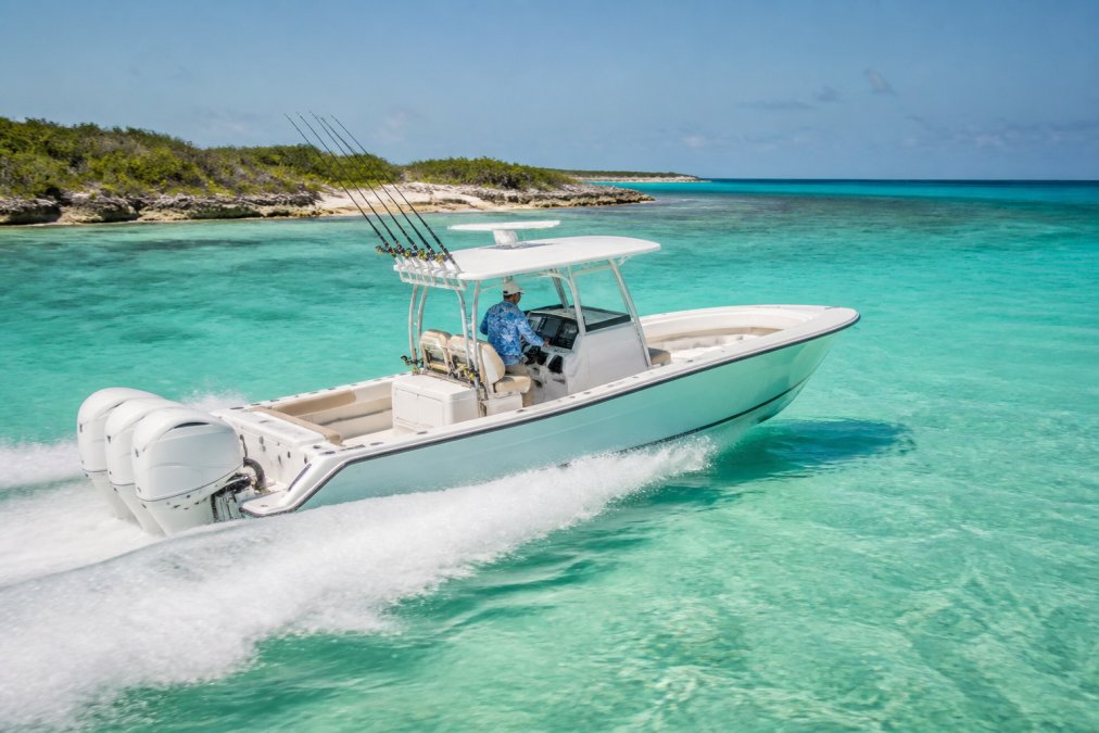 A center console boat running at speed across clear turquoise shallow water near a low-lying tropical island, with fishing rods rigged in rod holders and an angler at the helm station under bright midday sun