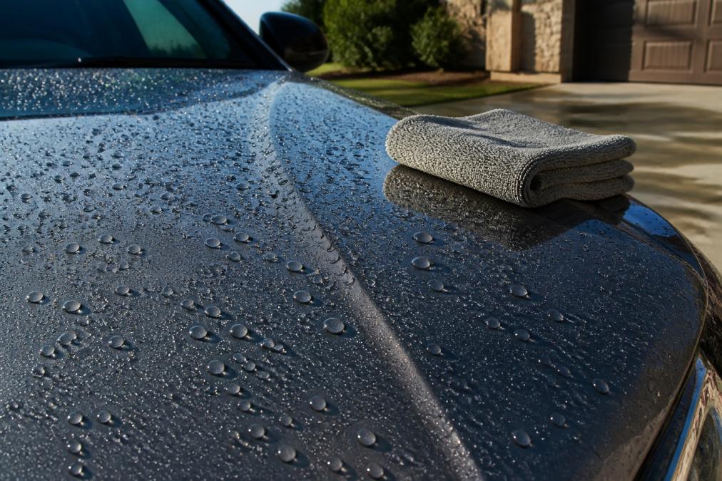 Water beading on a glossy car hood compared in a ceramic coating vs wax test on a driveway.