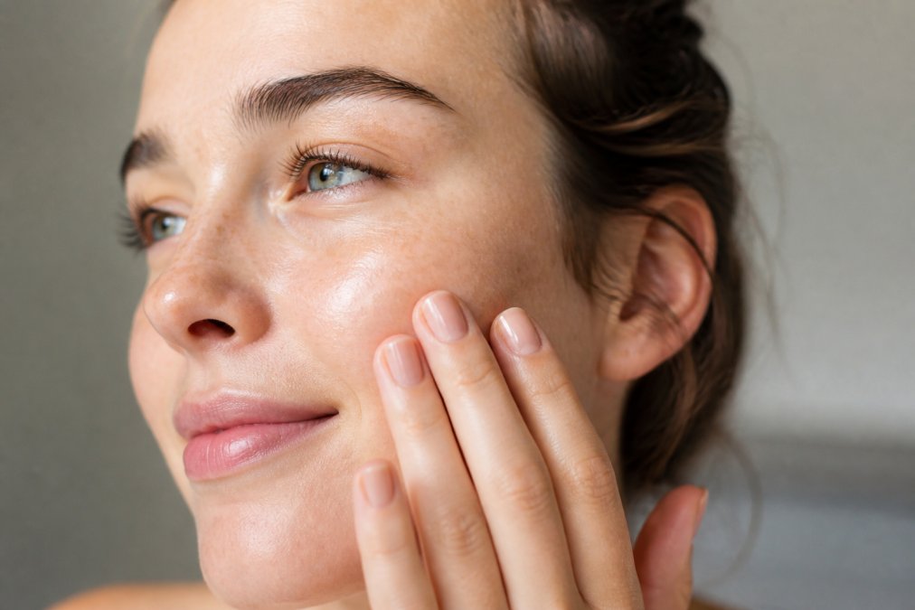 Close-up of a person's face showing calm, healthy skin with visible radiance, hands gently touching the cheek to demonstrate barrier health and hydration