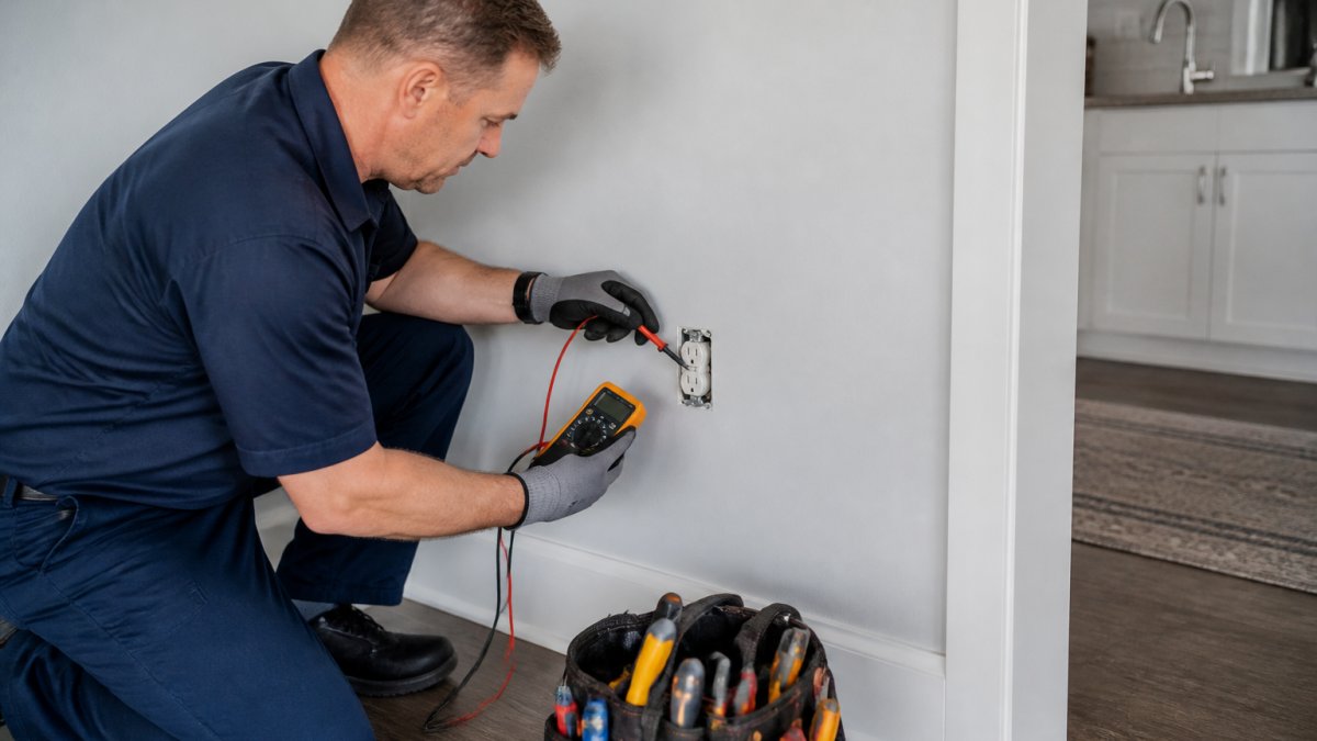Licensed electrician using a multimeter to verify electrical wiring code compliance in a residential home.