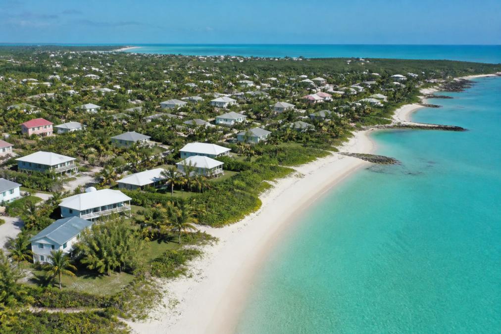 Aerial view of a quiet coastal town with white sand beach, calm turquoise water, and scattered residential properties nestled among palm trees and natural vegetation