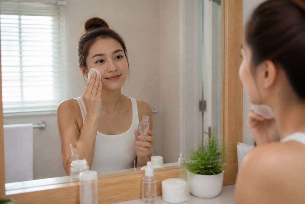 Woman applying glycolic acid to her face as part of chemical exfoliation vs physical scrubs skincare routines.