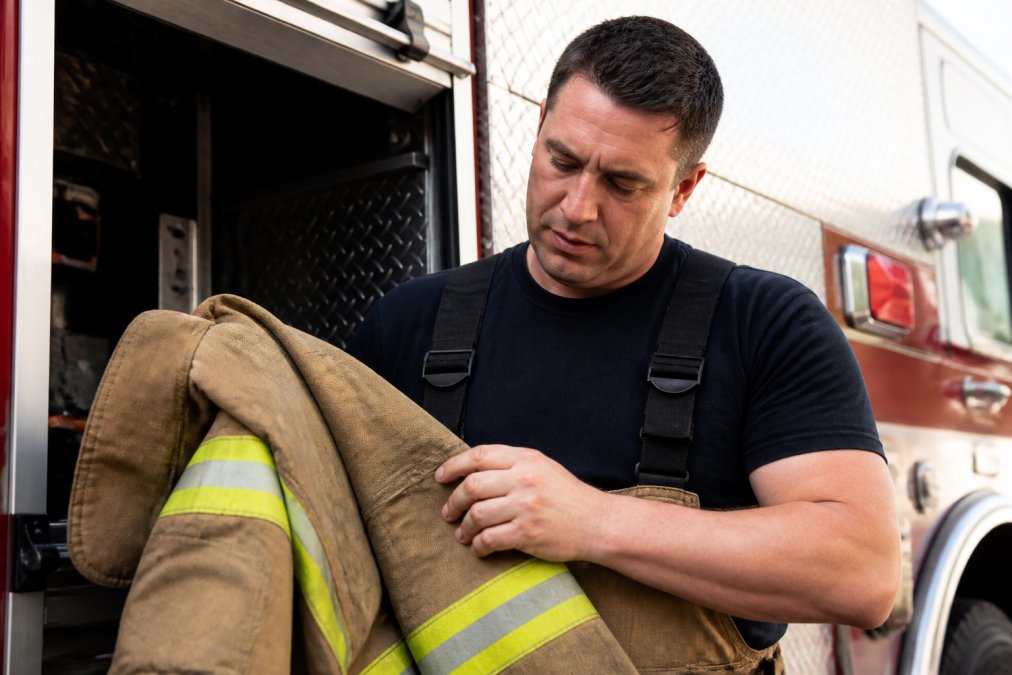 Close-up of firefighter examining premium apparel fabric texture, running fingers across weave quality and construction details in natural daylight