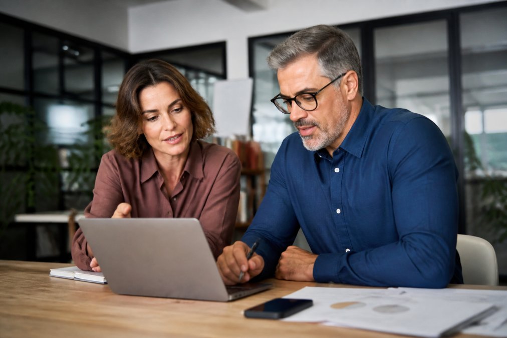 Small business owner and fractional CMO reviewing marketing strategy and performance metrics on a laptop during a collaborative strategy session in a modern office