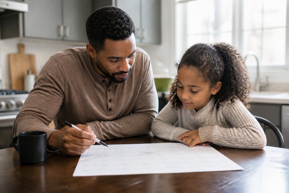 Parent and child at kitchen table together reviewing a calendar or schedule, warm natural lighting showing routine and planning, both focused and calm