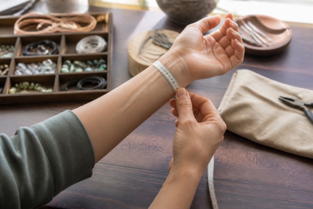 Close-up of hands using a soft measuring tape around a wrist, demonstrating proper bracelet sizing technique with the tape positioned just above the wrist bone