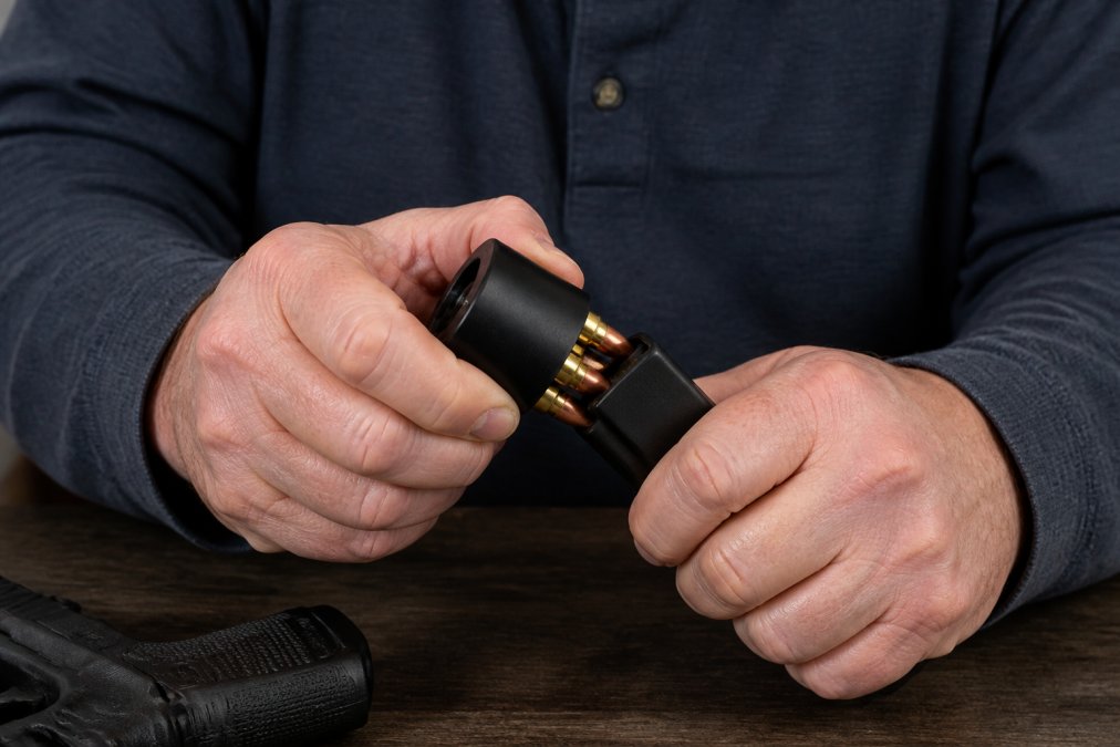 Close-up of hands demonstrating proper grip and positioning on a speed loader with relaxed finger placement and wrist alignment, showing how to minimize joint stress during magazine loading