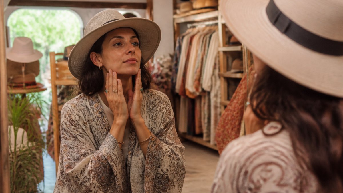 Woman examining her face in a mirror, gently tracing her jawline and cheekbones with her fingers to identify facial contours and proportions