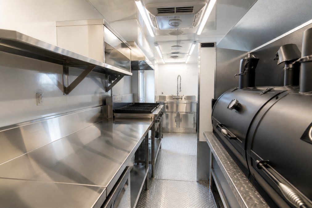 Stainless steel prep station inside a catering trailer with a clear workflow path to the smoker and sink area.