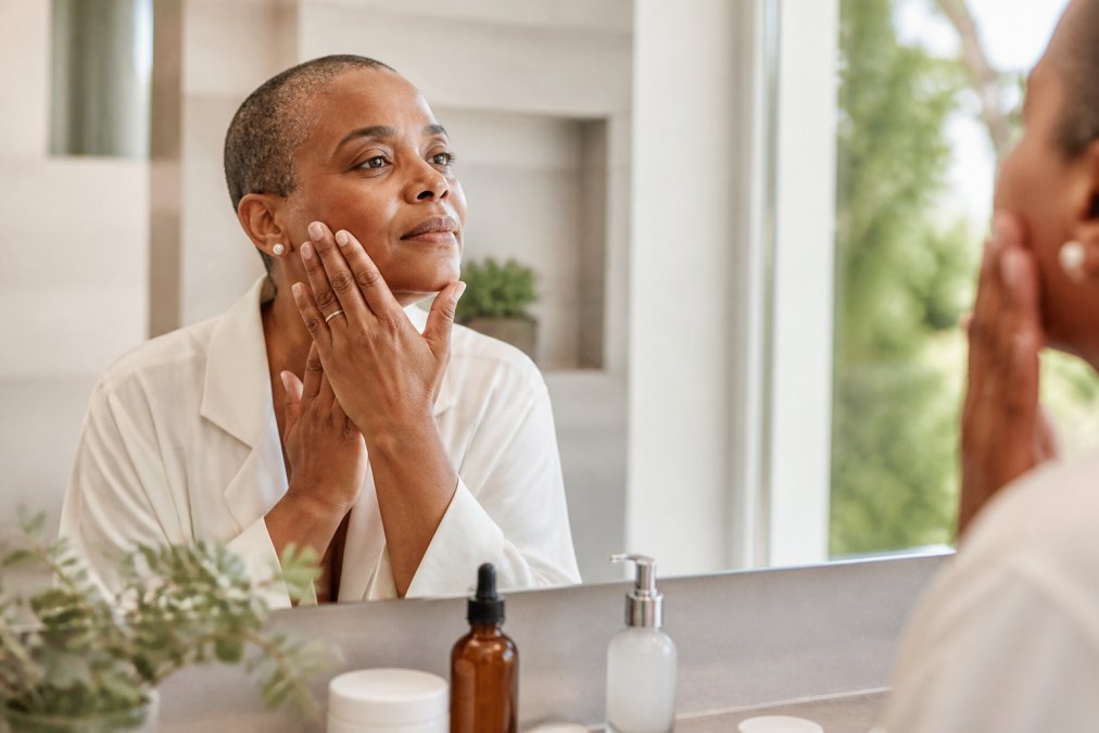 Woman with short hair gently applying fragrance-free moisturizer to her face in a calm, sunlit bathroom