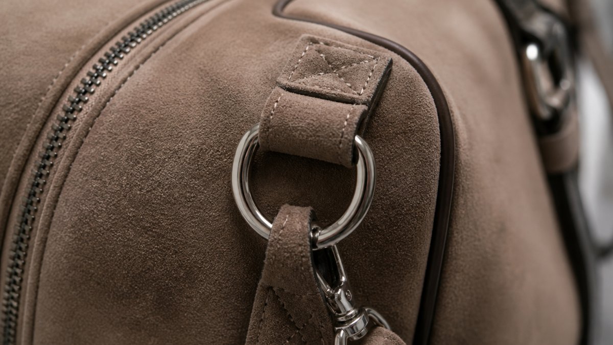 Close-up of premium Ultrasuede fabric texture showing rich color depth with reinforced stitching and polished metal hardware on luxury dog carrier surface