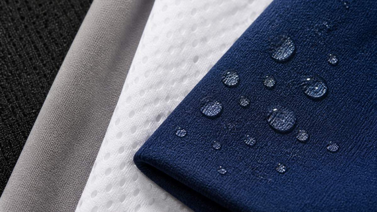 Close-up of sports jersey fabric samples showing different weaves and textures, with water beading on polyester blend material to demonstrate quick-drying properties