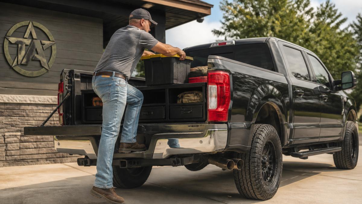 Truck owner using side step to safely load cargo into pickup bed in daylight, with organized toolbox visible