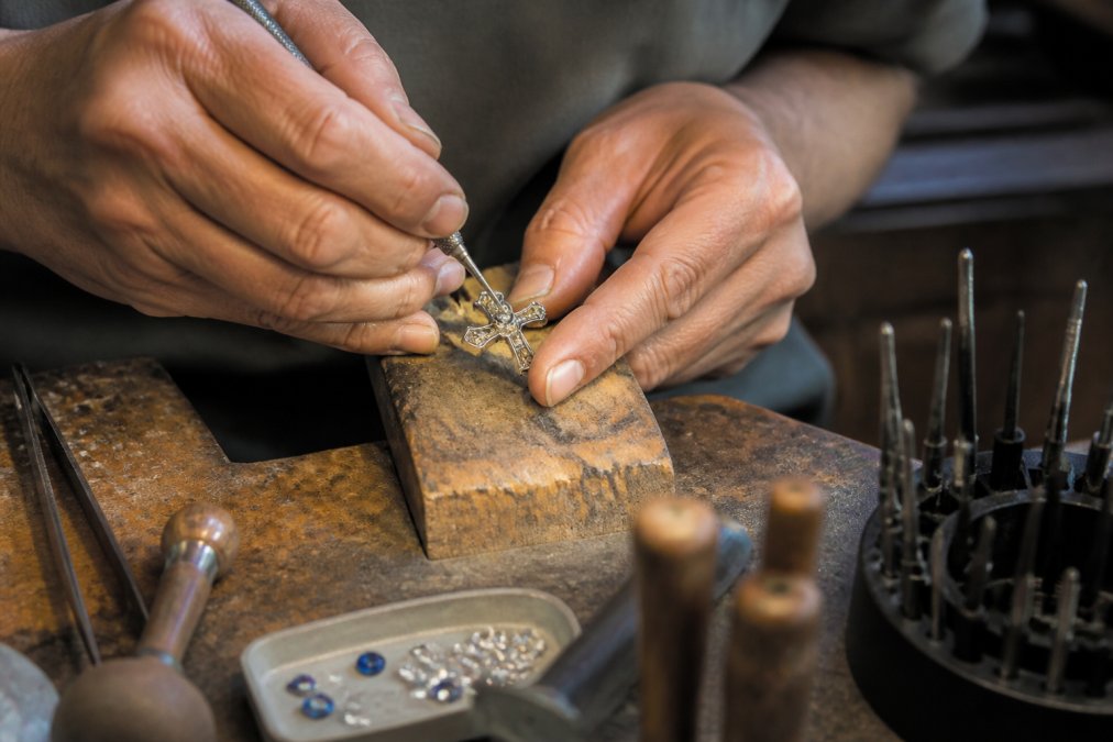 Artisan hands carefully setting a gemstone into a silver cross pendant for handcrafted christian jewelry