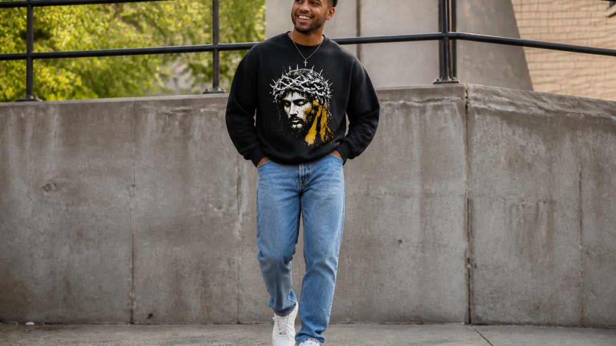 Young person wearing a graphic faith sweatshirt and jeans in an urban setting