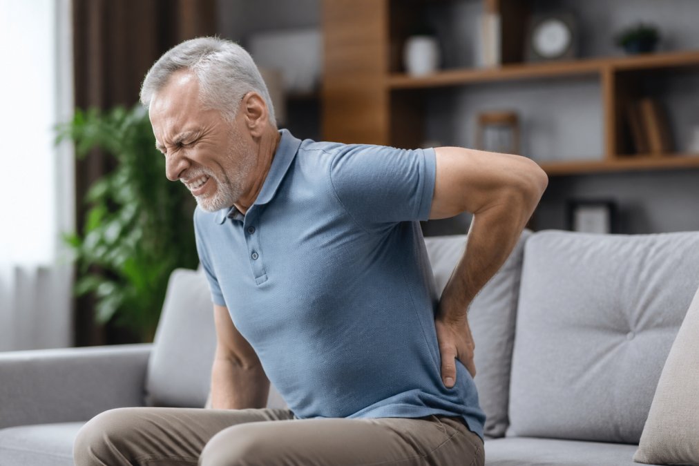 Person holding lower back in visible discomfort, demonstrating the physical experience of chronic pain and inflammation connection, with natural indoor lighting