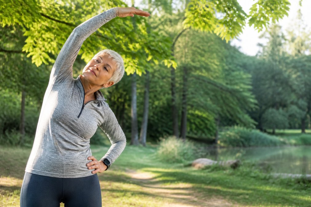 Active older adult performing gentle stretching outdoors in natural morning light, demonstrating movement and wellness practices for reducing chronic pain and inflammation