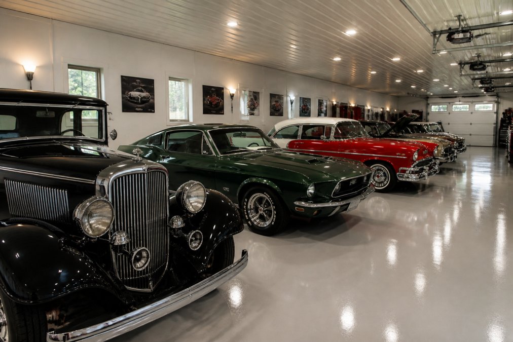 Multiple classic cars parked side-by-side in a climate-controlled garage with proper lighting, showcasing a well-organized collector's vehicle collection