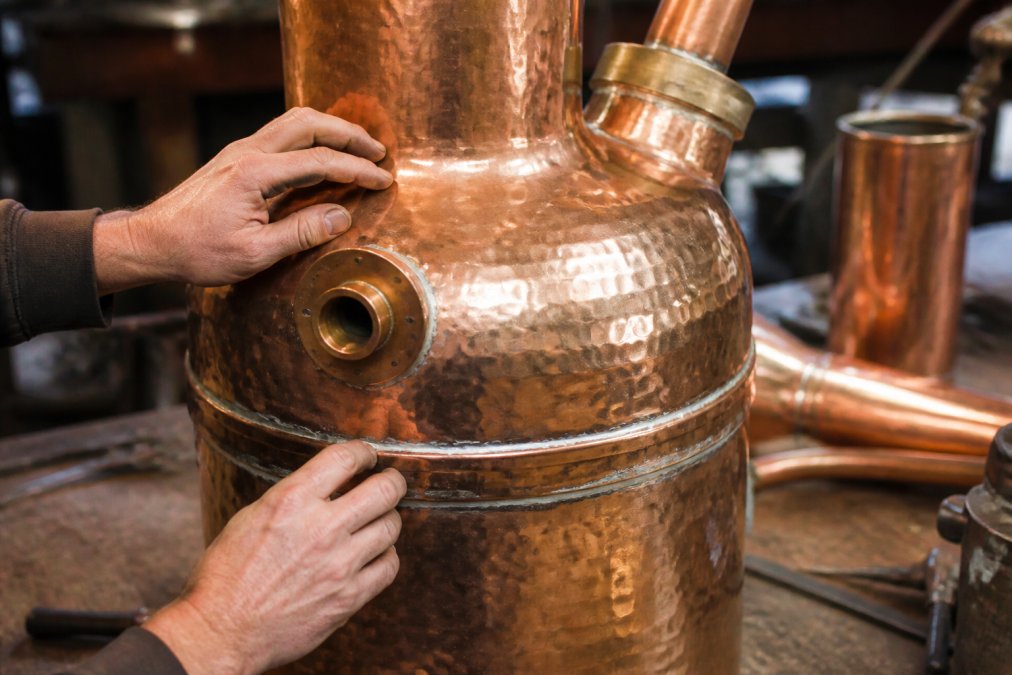 Hand-made copper still with hammered texture as a durable clawhammer supply alternative on a workbench