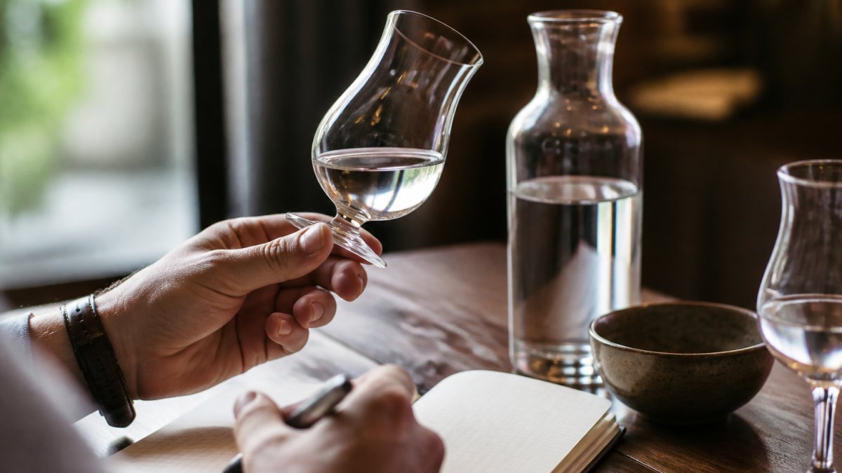 Hands holding a crystal glass to inspect tequila clarity and color with tasting notes on a nearby table