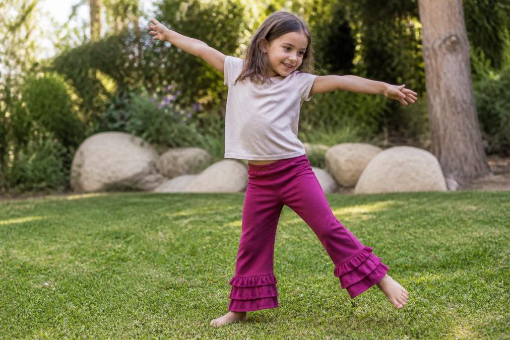 Child wearing soft bamboo ruffle pants in berry color, stretching and moving freely while playing outdoors, showing comfortable fit and ease of movement with relaxed posture